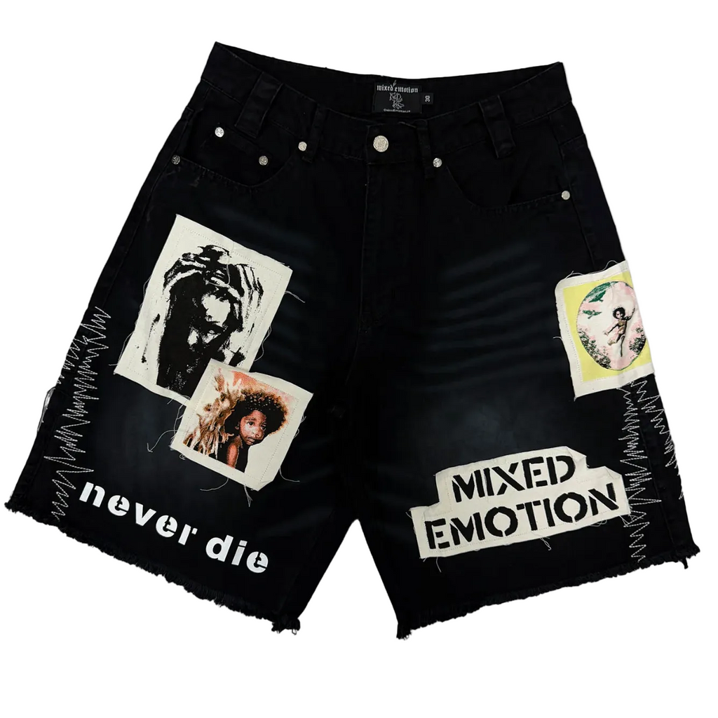 Black denim shorts with distressed frayed hems, featuring graphic patches, ripped paper-style overlays reading 'never die' and 'MIXED EMOTION', and two portrait stickers on the front, shown on a plain white background.