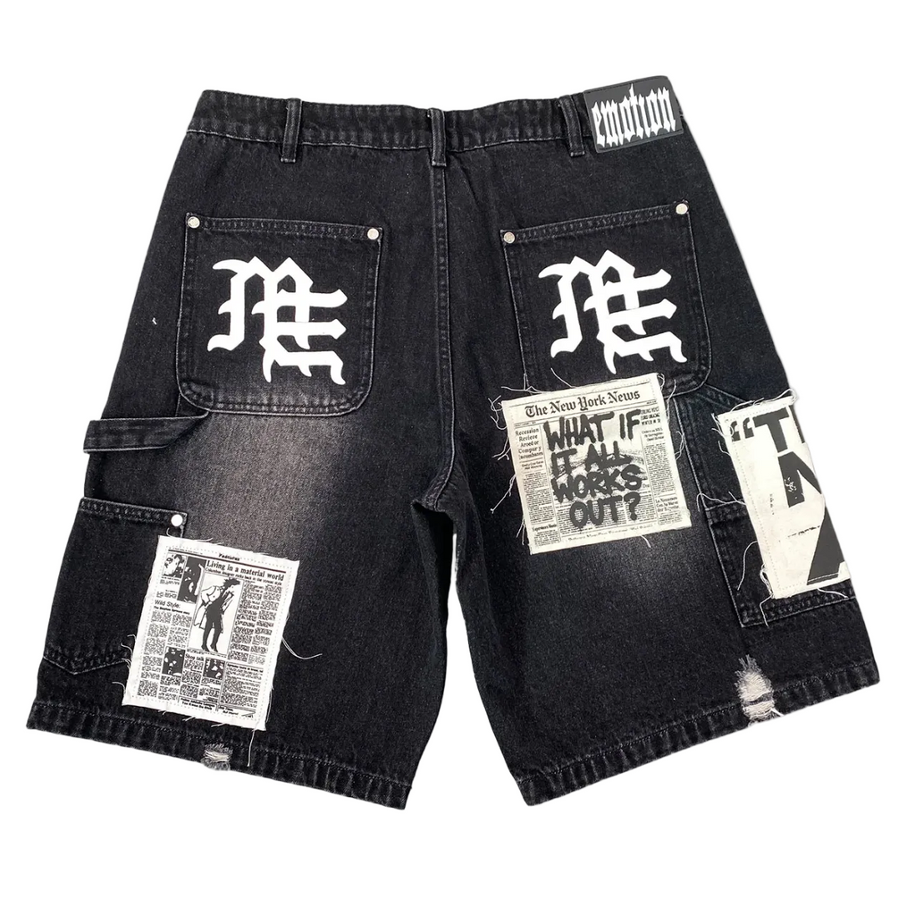 Black washed denim cargo shorts with multiple graphic patches and white gothic lettering on the back pockets, shown flat on a white background.